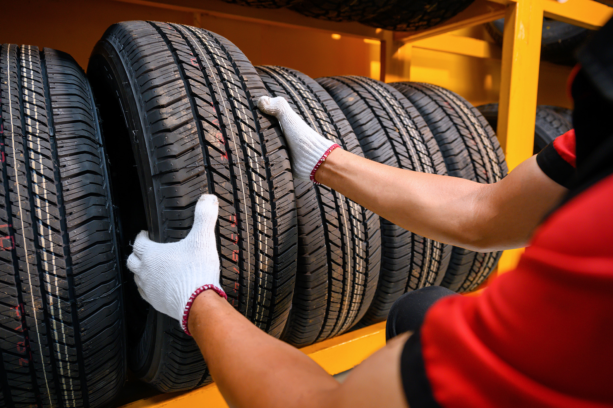 Person wearing white gloves organizing new tires on a yellow metal rack.