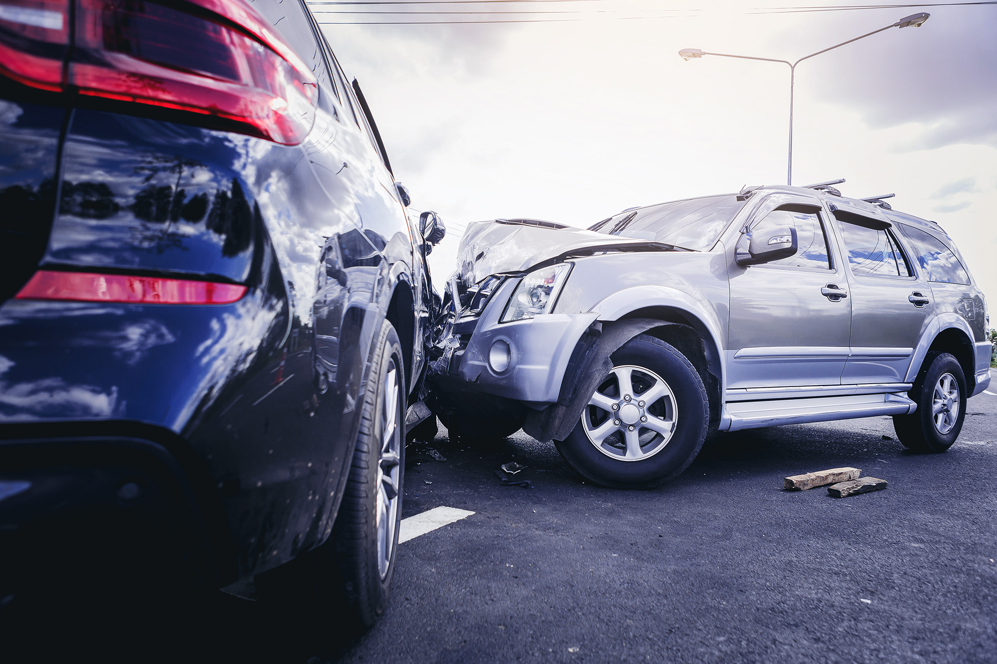 Silver SUV with front-end damage collided with black car on an asphalt road under a cloudy sky.