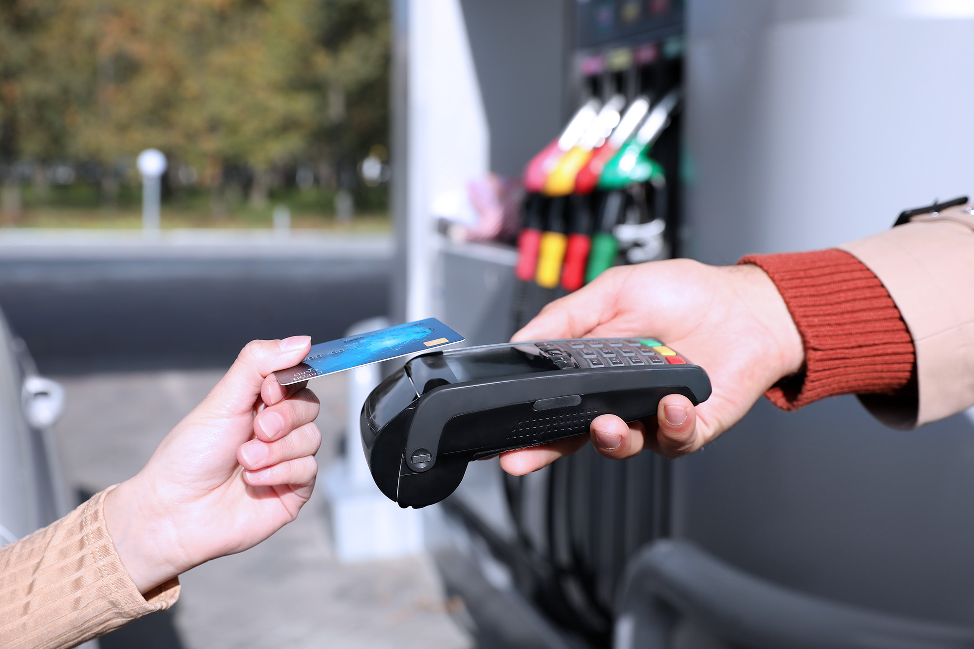 Person holding a credit card near a payment terminal at a gas station fuel pump.