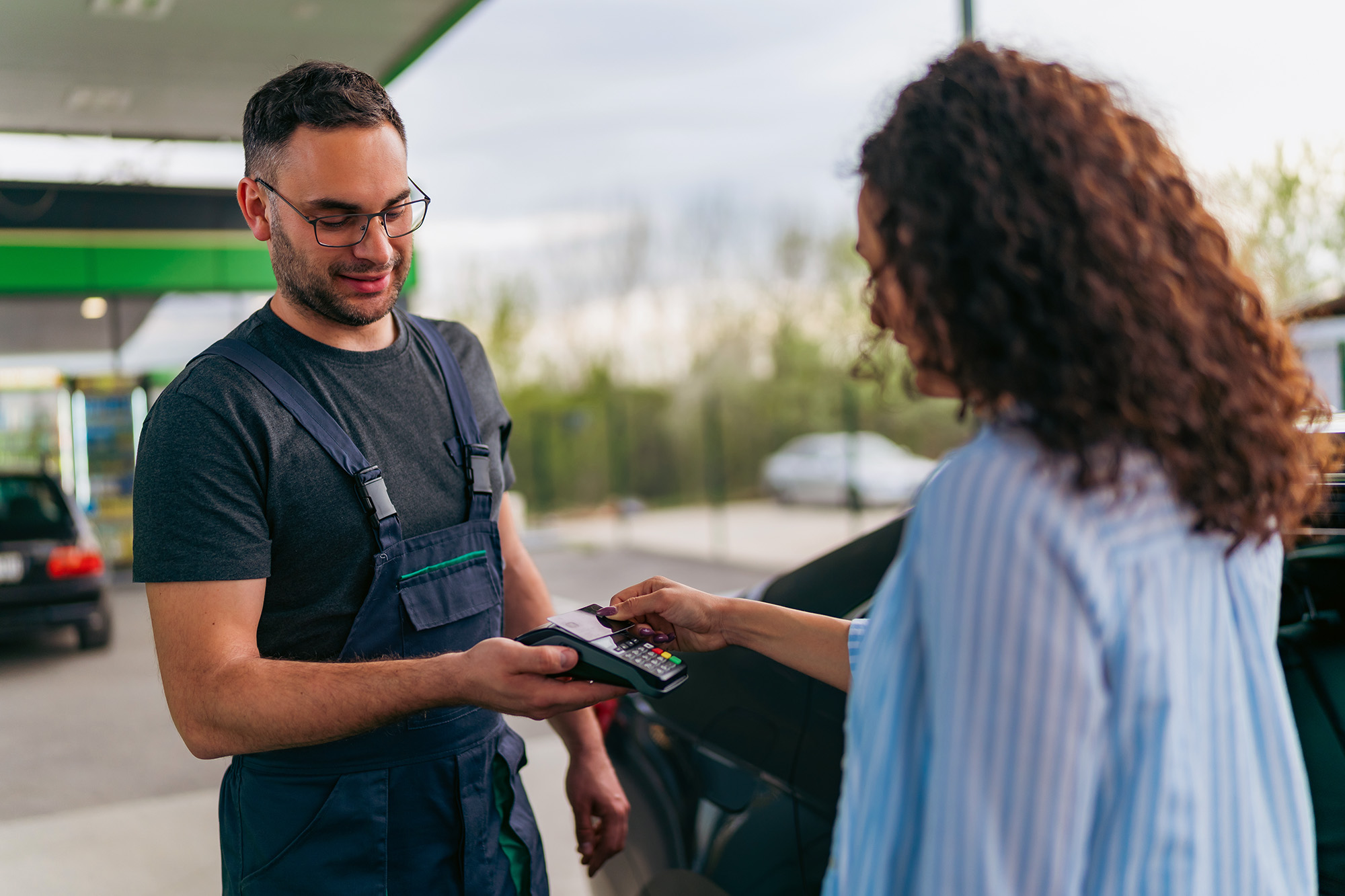 Woman making a contactless payment with a card reader held by a gas station attendant.