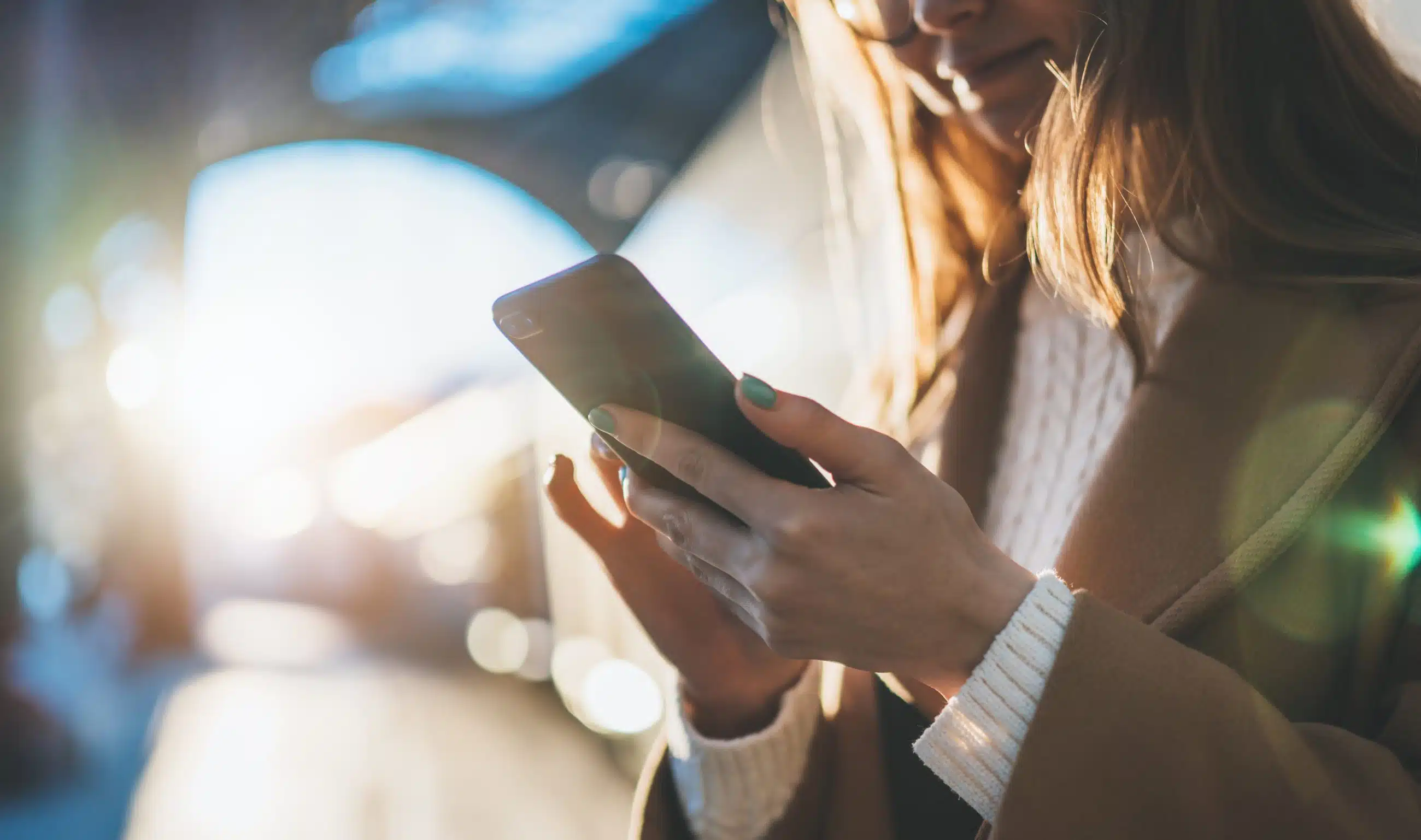 Close-up of a woman holding and using a smartphone with natural sunlight in the background.
