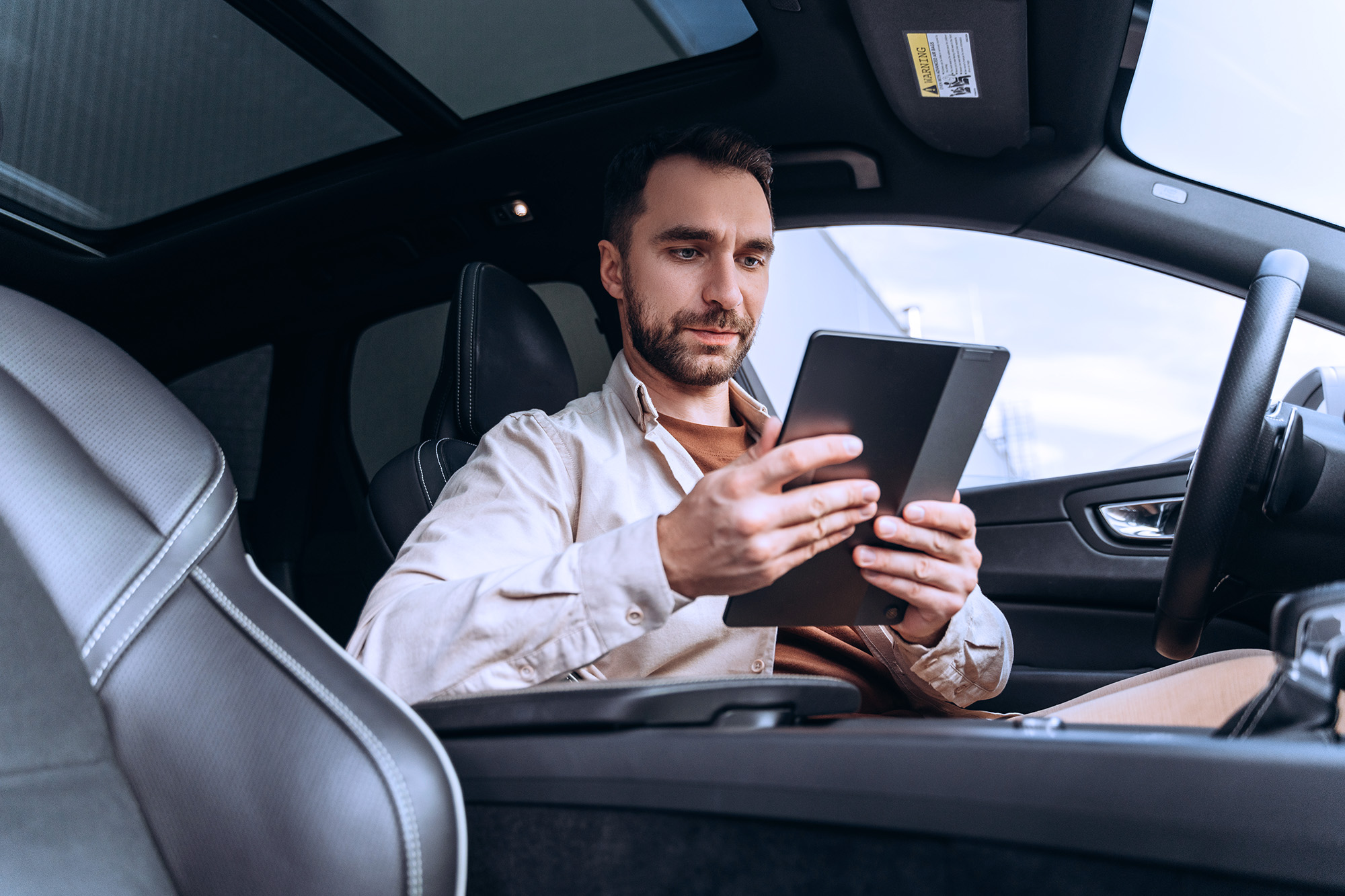Man sitting in the driver's seat of a car looking at a tablet device.