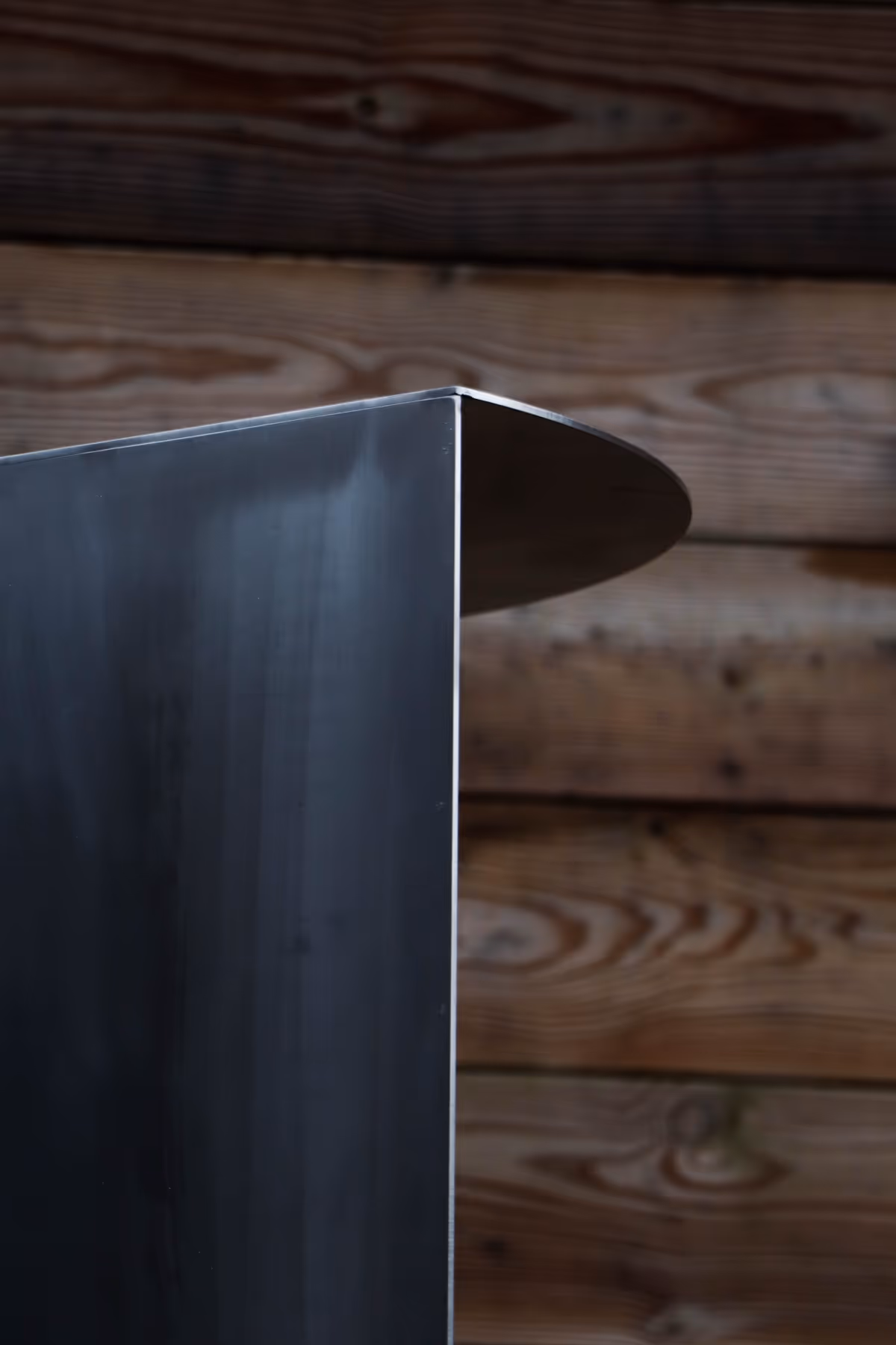Close-up of a sleek black metal object with a rounded edge against a wooden plank background.