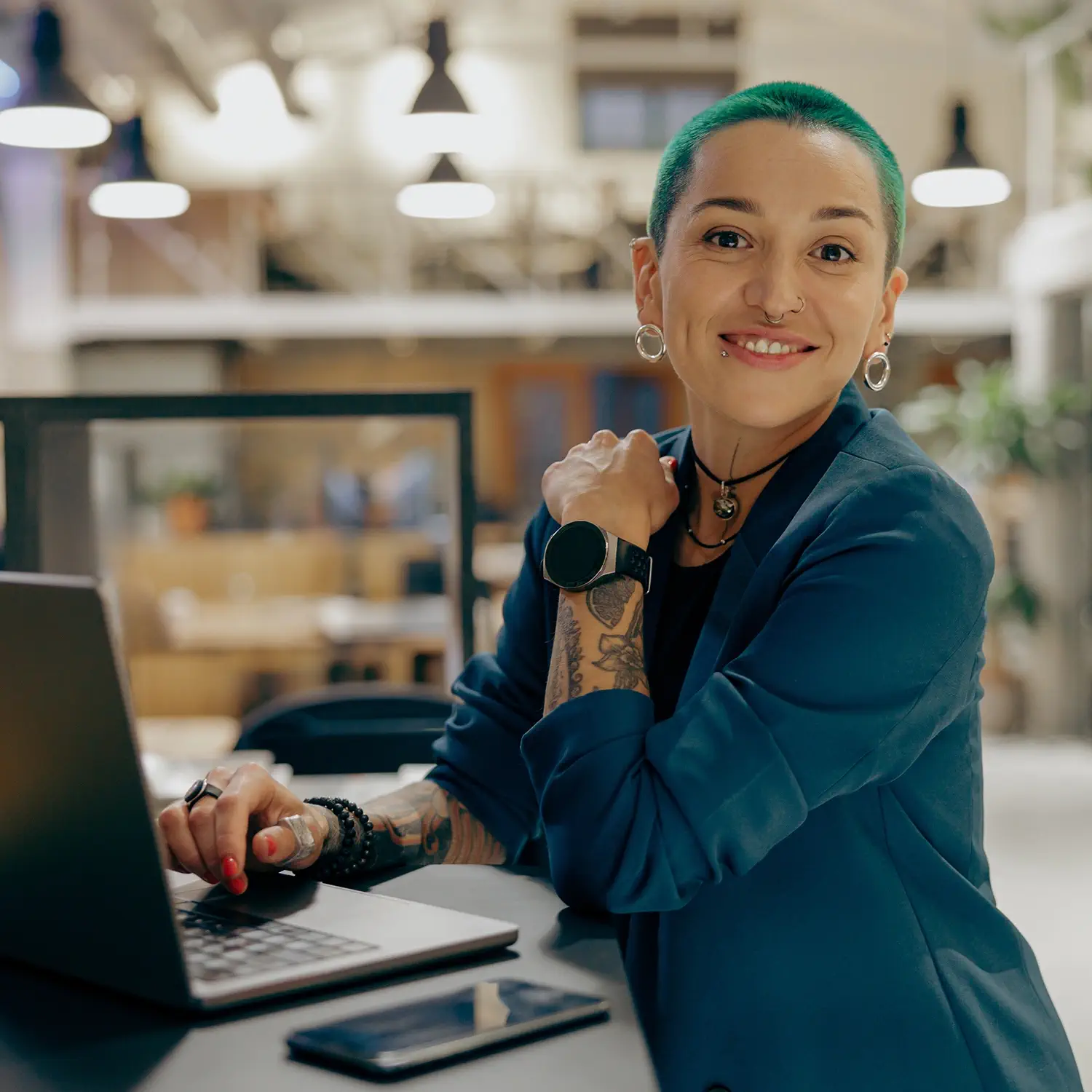 Individuelle Benefits für moderne Talente: Eine lächelnde Frau mit grünen Haaren arbeitet an einem Laptop von DVICE – das Mitarbeiter-PC-Programm der JobRad Gruppe stärkt die Arbeitgeberattraktivität durch modernste Technik und freie Hardware-Wahl.