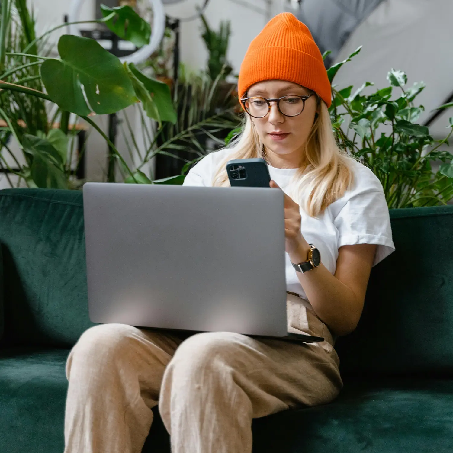 Flexibles Arbeiten im modernen Homeoffice: Eine Frau mit Brille und Beanie nutzt Laptop und Smartphone von DVICE – das digitale Mitarbeiter-PC-Programm der JobRad Gruppe ermöglicht den Zugang zu aktuellster Technik als attraktiven Mitarbeiterbenefit per Gehaltsumwandlung.