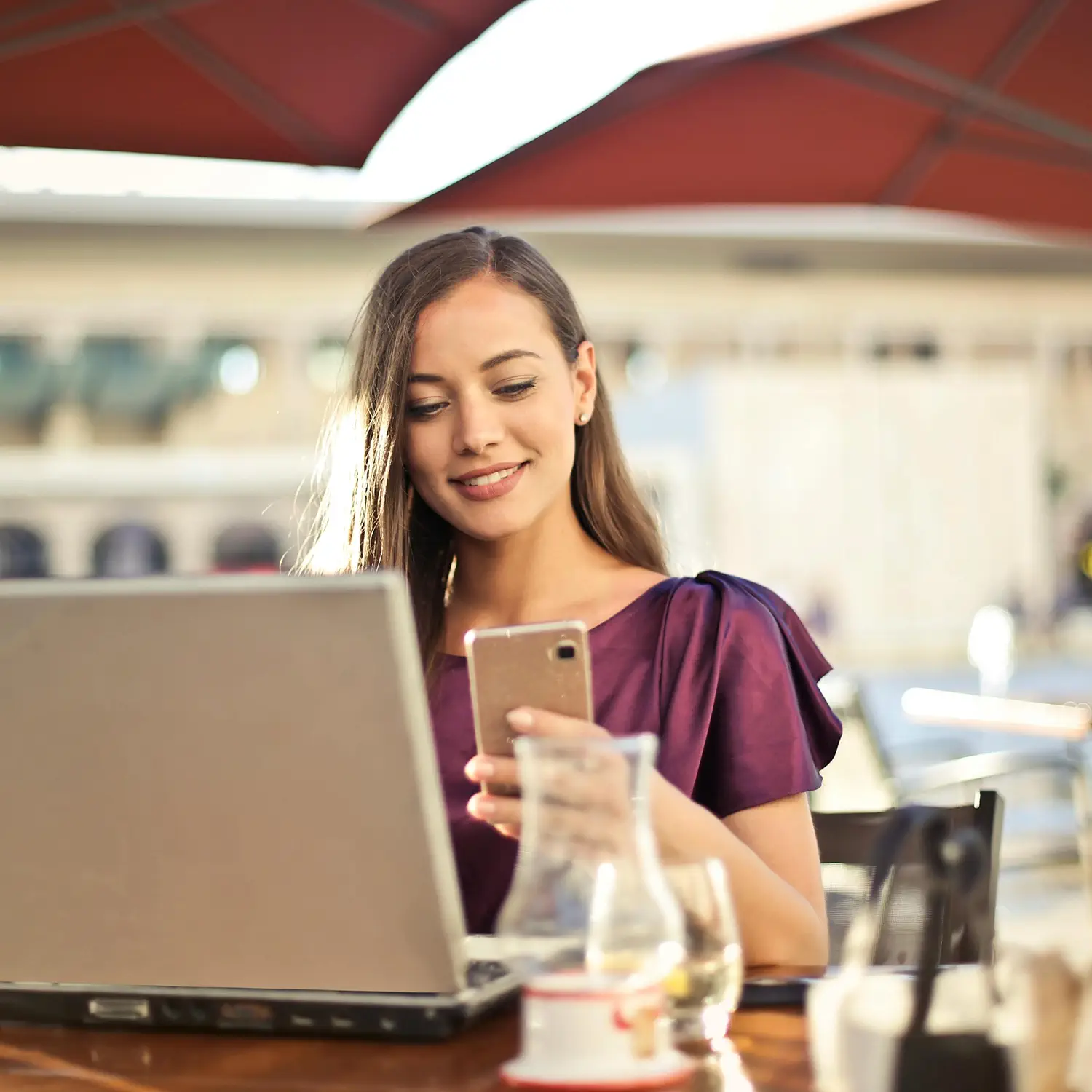 Flexibler Technik-Lifestyle an jedem Ort: Eine Frau nutzt Smartphone und Laptop in einem Café – ermöglicht durch das DVICE Mitarbeiter-PC-Programm der JobRad Gruppe mit bis zu 30 % Ersparnis durch Gehaltsumwandlung.
