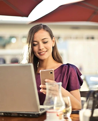 Flexibler Technik-Lifestyle an jedem Ort: Eine Frau nutzt Smartphone und Laptop in einem Café – ermöglicht durch das DVICE Mitarbeiter-PC-Programm der JobRad Gruppe mit bis zu 30 % Ersparnis durch Gehaltsumwandlung.