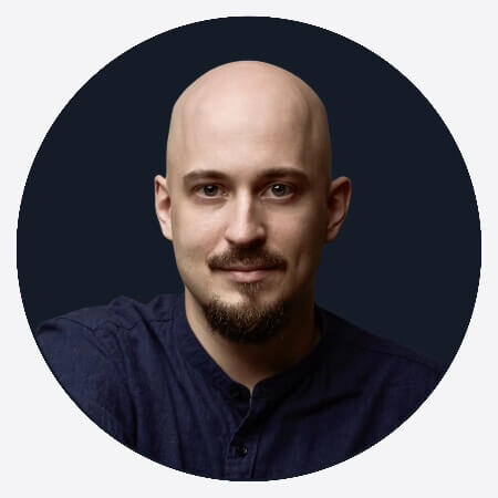 Portrait of a bald man with a short beard and mustache wearing a dark shirt against a black circular background.