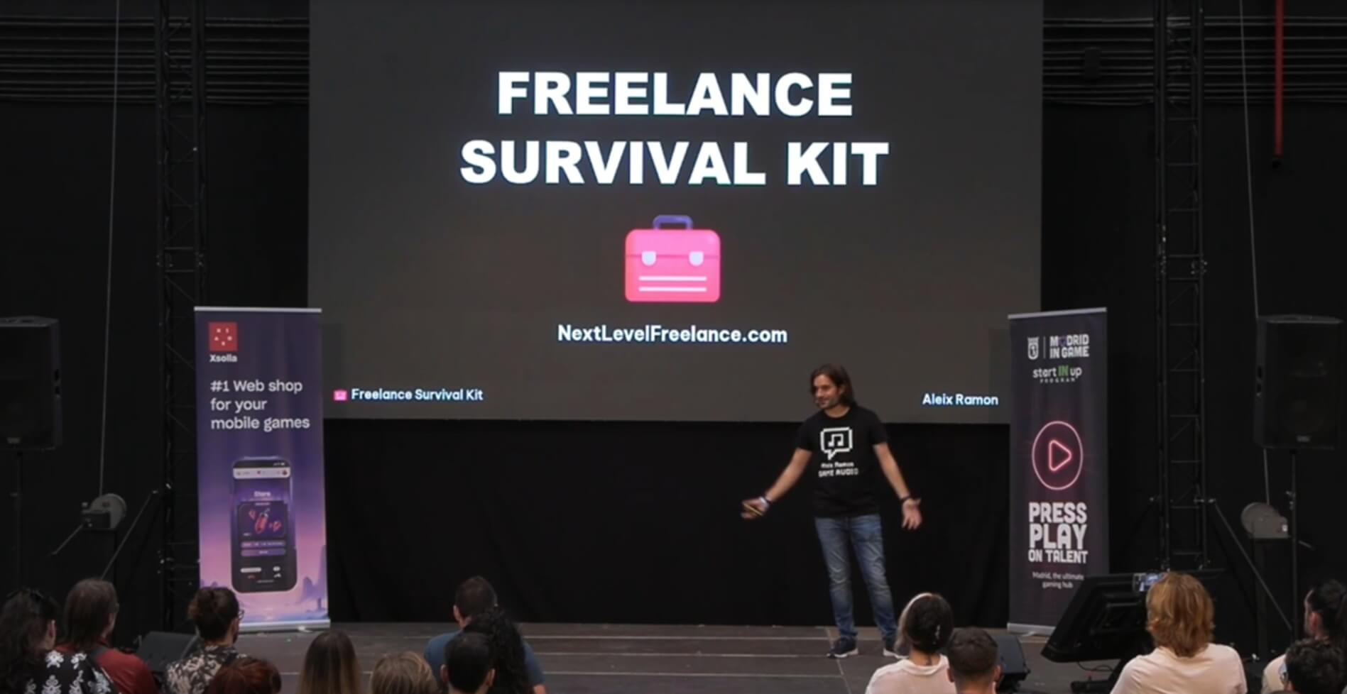 Speaker Aleix Ramon presenting on stage with a screen behind him displaying 'FREELANCE SURVIVAL KIT' and the URL NextLevelFreelance.com, with an audience watching.