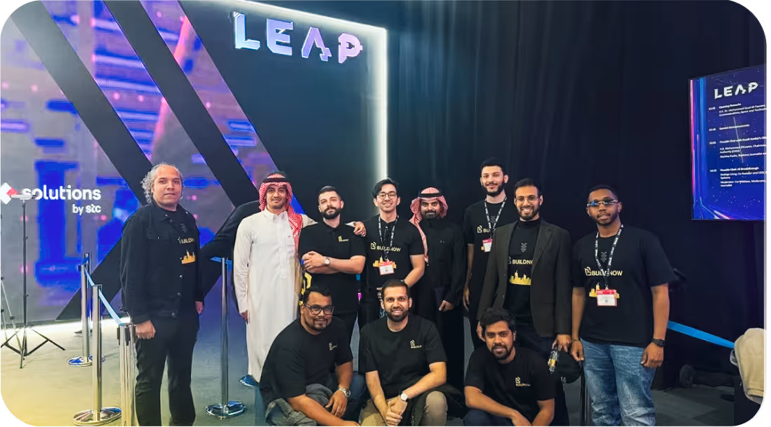 مجموعة من الرجال يقفون يبتسمون في حدث LEAP مع شعار BuildNow وشعار solutions by stc في الخلفية.