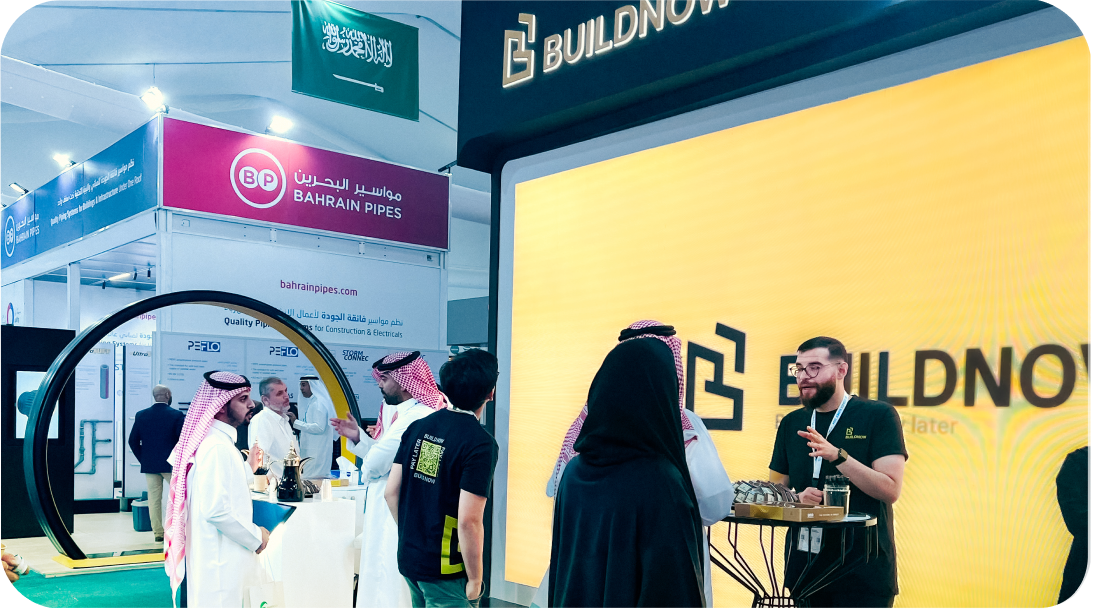 أشخاص يرتدون الأزياء التقليدية في معرض تجاري أمام أكشاك تحمل شعارات شركات بناء وأنابيب البحرين.