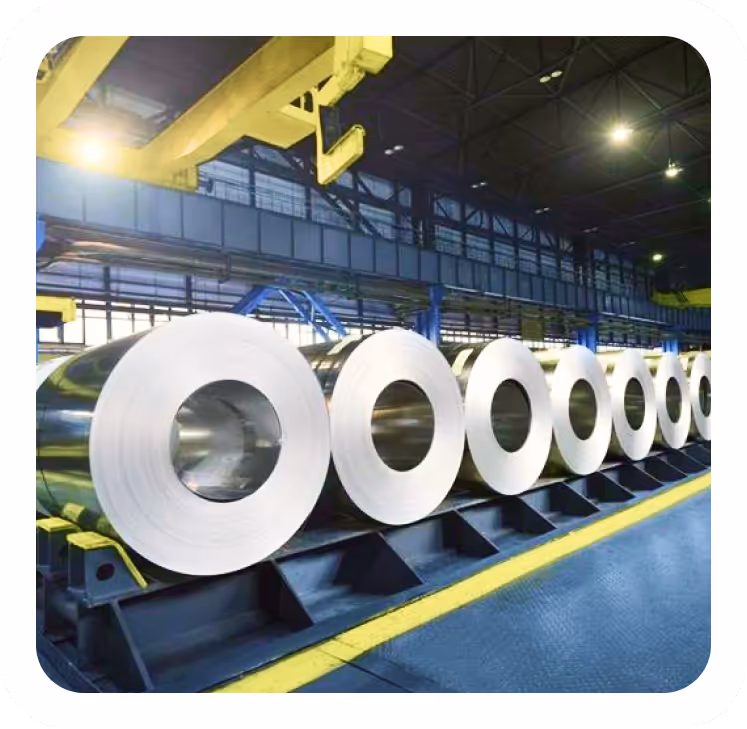 لفائف من الصلب اللامع مصطفة في مصنع صناعي تحت إضاءة صناعية.