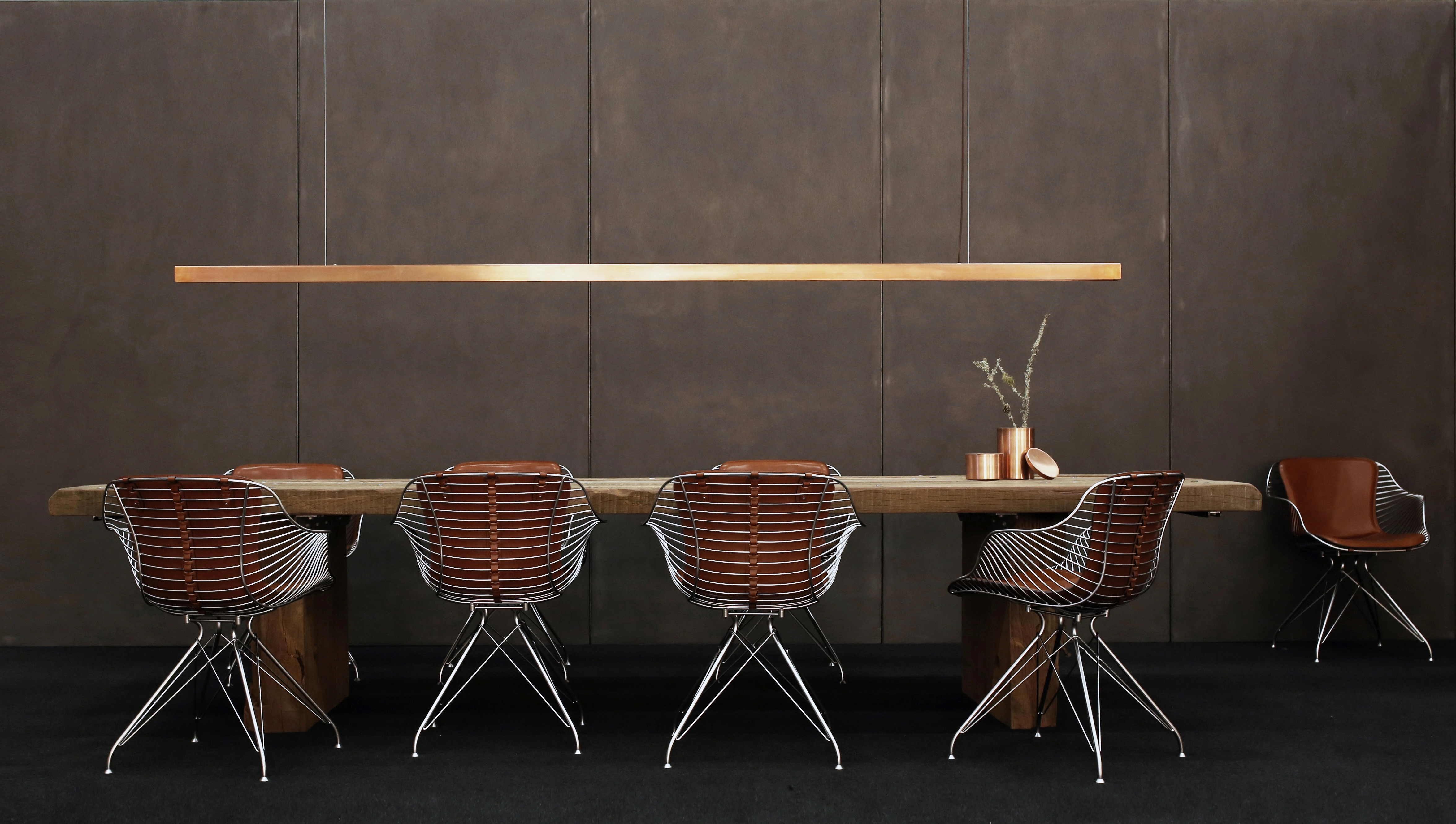 Modern dining room with a wooden table, five wireframe chairs with brown cushions, and a slim horizontal pendant light above.