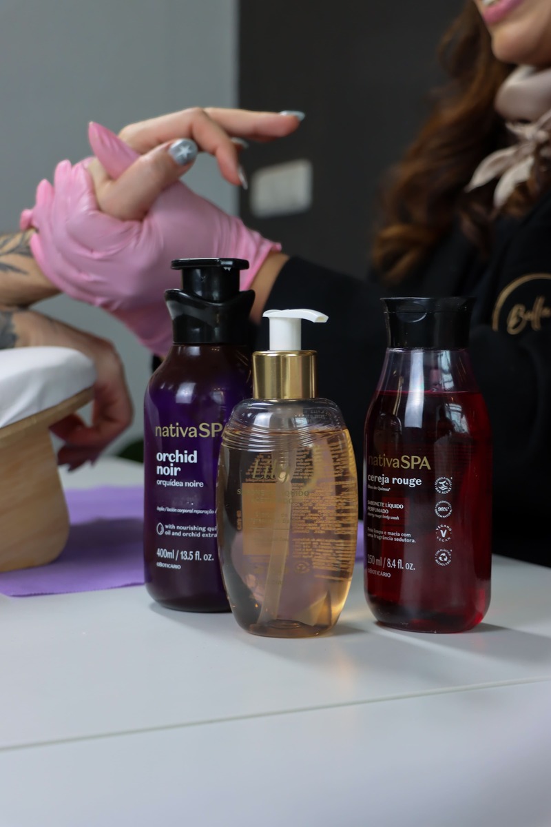 Drei Flaschen mit Spa-Hautpflegeprodukten stehen auf einem Tisch, im Hintergrund hält eine Person mit rosa Handschuhen die Hand einer anderen Person.