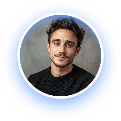 Portrait of a young man with short curly dark hair and a slight beard, wearing a black sweater, against a gray blurred background.