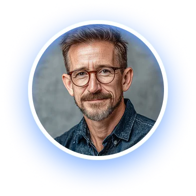 Middle-aged man with short hair, beard, and glasses wearing a dark denim shirt smiling against a gray background.