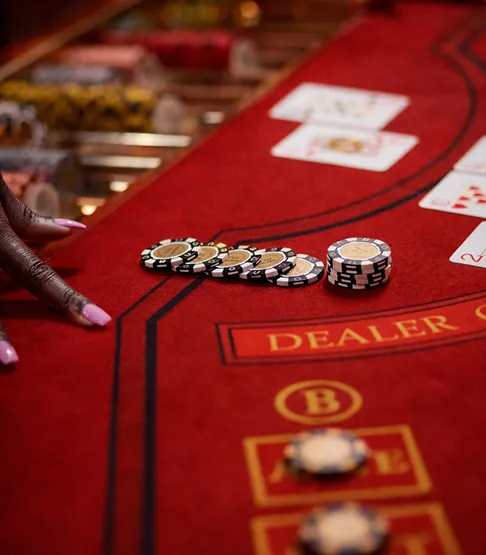 A hand with pink-painted nails placing casino chips on a red felt blackjack table with cards visible.