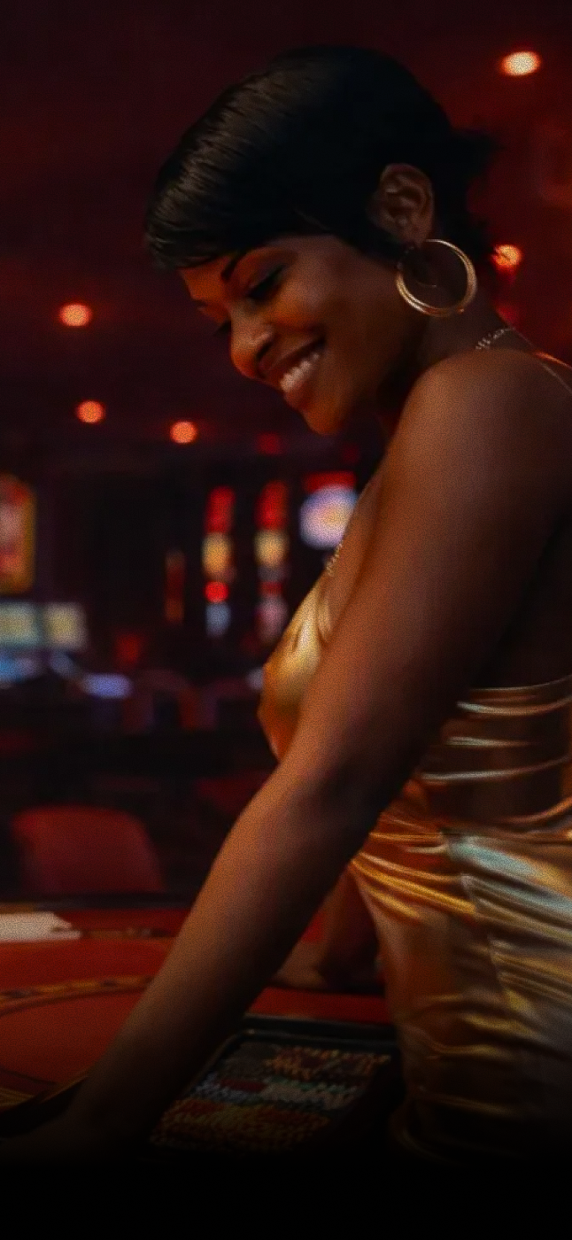 Woman in a gold dress leaning on a casino table with blurred slot machines in the background.