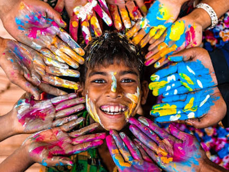A young smiling boy surrounded by brightly coloured painted hands