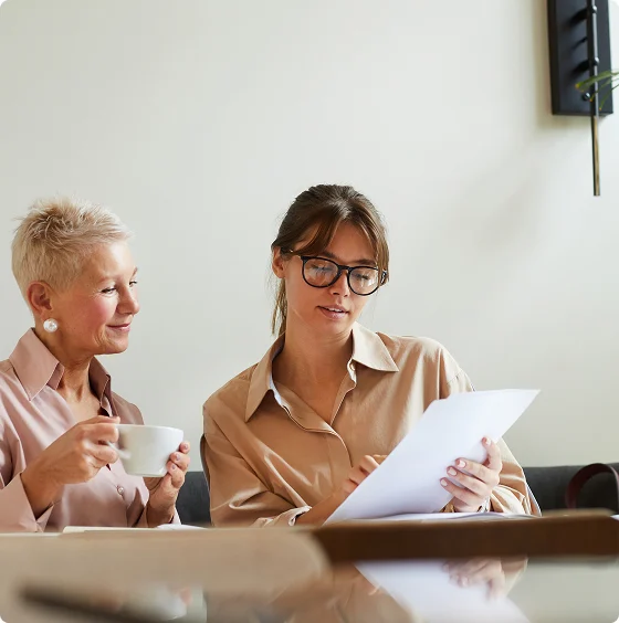 Smiling older woman sitting cross-legged on a sofa using a smartphone, with illustrated plant, trophy, and lamp around her.