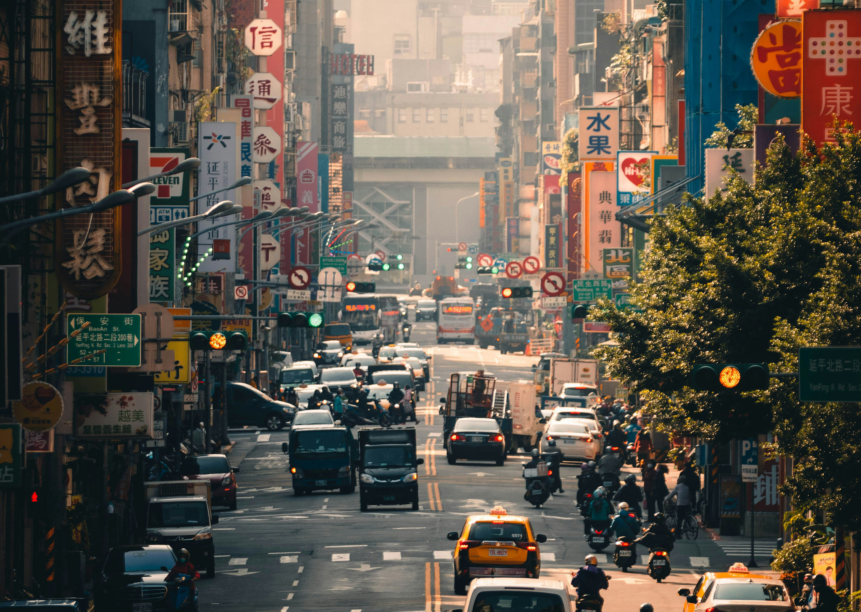 Busy urban street in Taipei with heavy traffic, scooters, cars, and colorful vertical signs in Chinese characters lining both sides.
