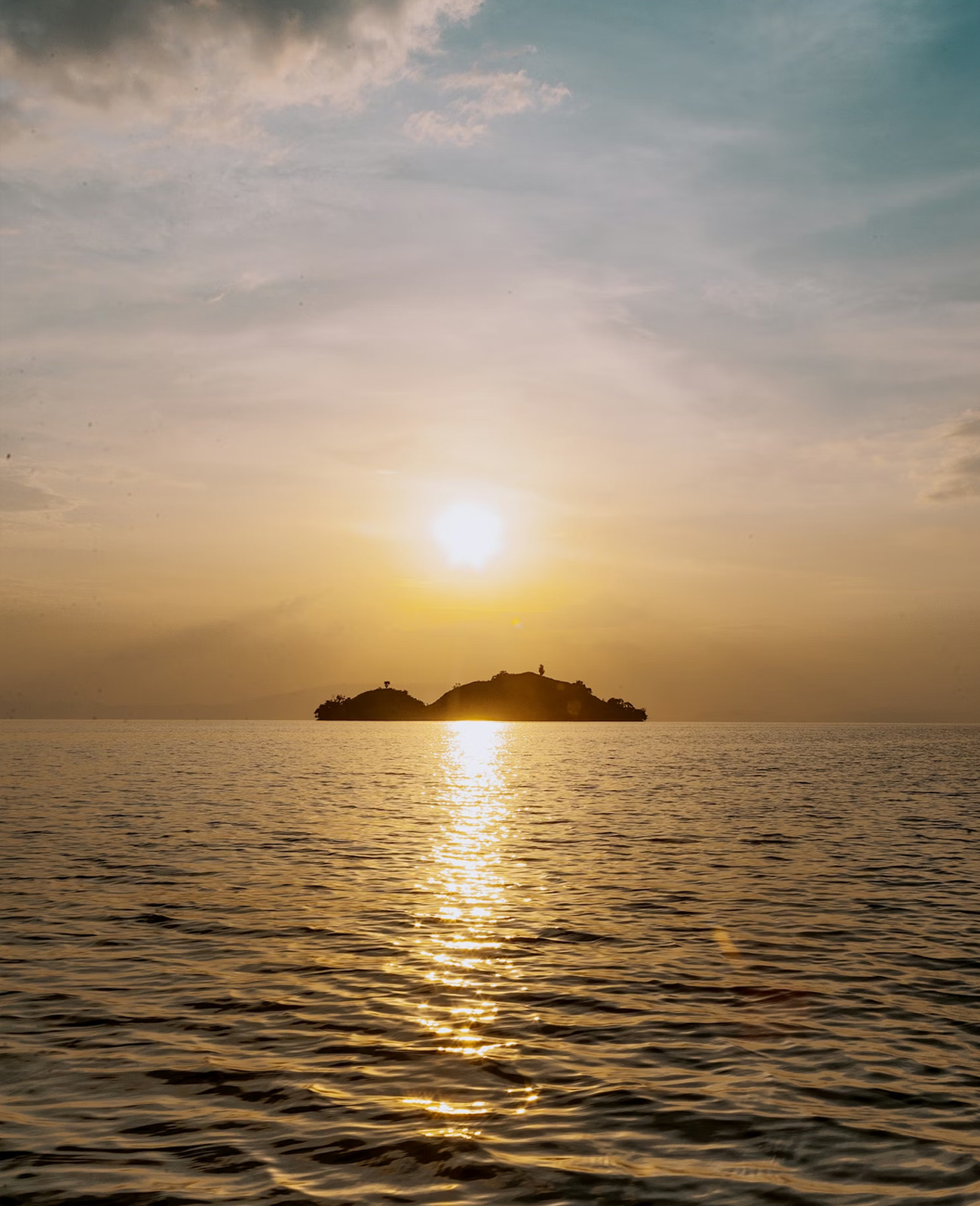 Sunset over a calm sea with a small silhouetted island reflecting golden light on the water.
