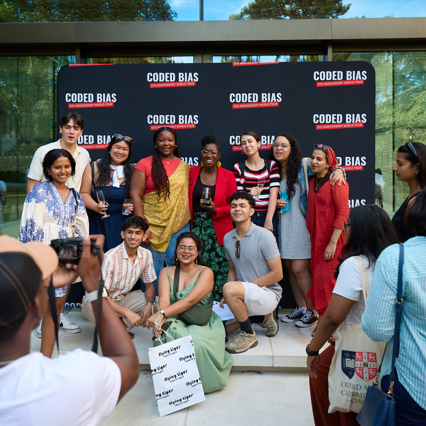 Four smiling women standing together in front of a 'Coded Bias 5th Anniversary World Tour' backdrop.