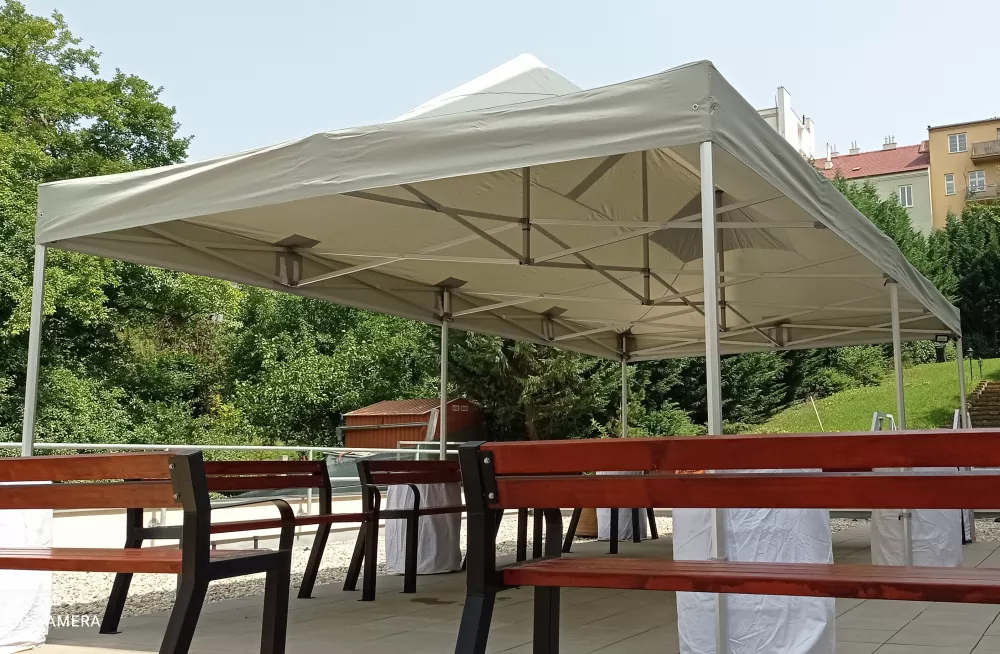 Šedý nůžkový stan 8×4 m bez bočních stěn zastřešující venkovní posezení s lavicemi