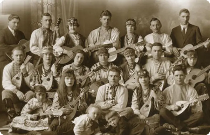 Sepia-toned vintage photo of a large group of people in traditional Eastern European folk costumes holding stringed folk instruments.