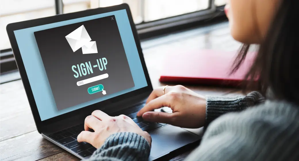 Person typing on a laptop displaying a sign-up form with an email input field and submit button.