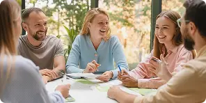 Four people sitting around a table engaged in a lively discussion, smiling and holding pens.