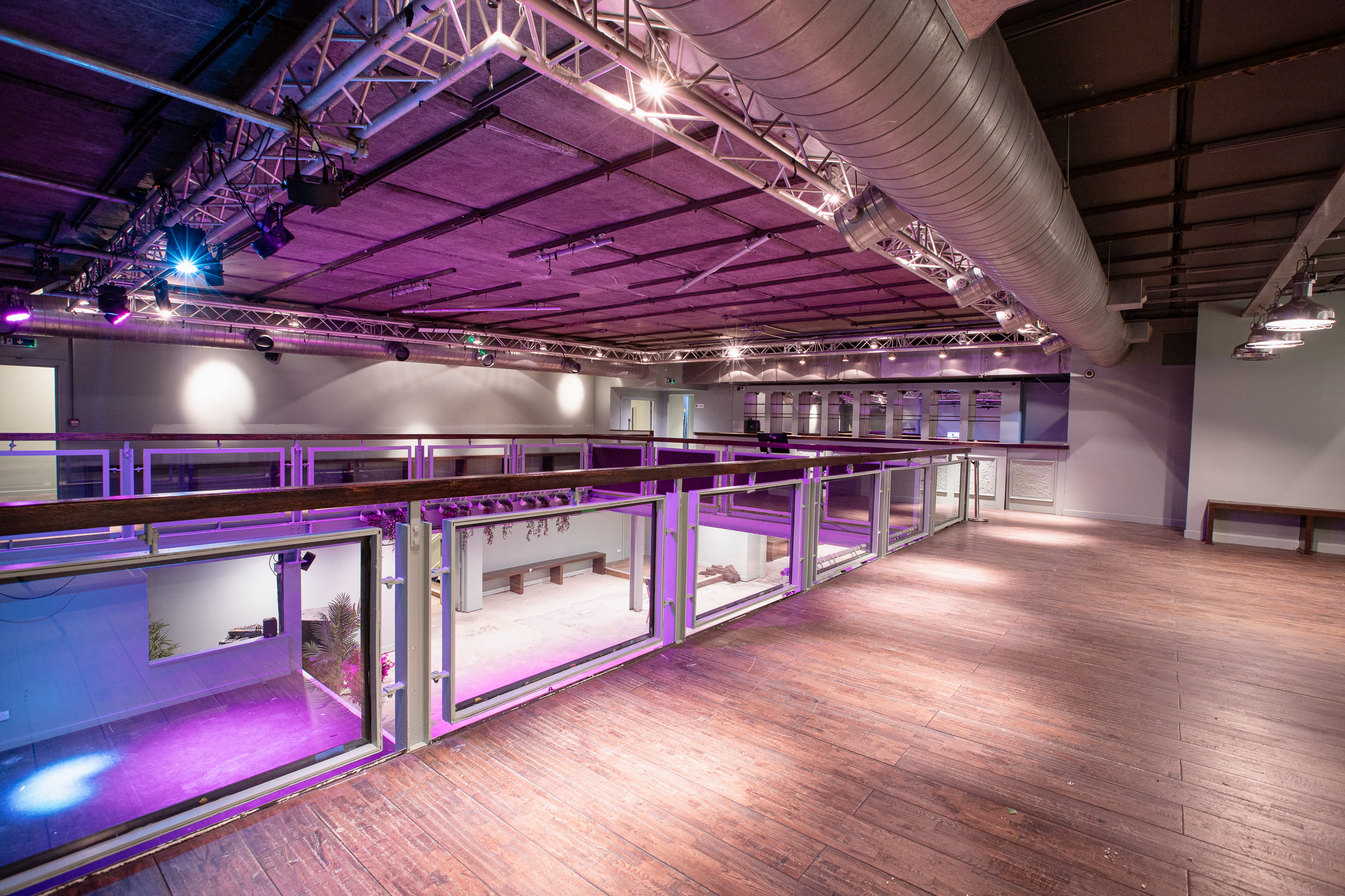 Spacious modern mezzanine with wooden floor, glass railing, and purple ambient lighting.