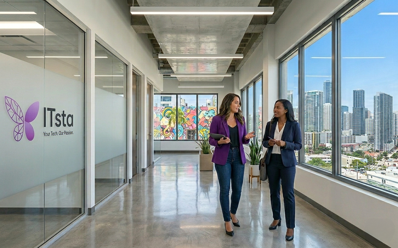 Two businesswomen walking and talking in a modern office hallway with large windows showing city skyscrapers and colorful wall art.