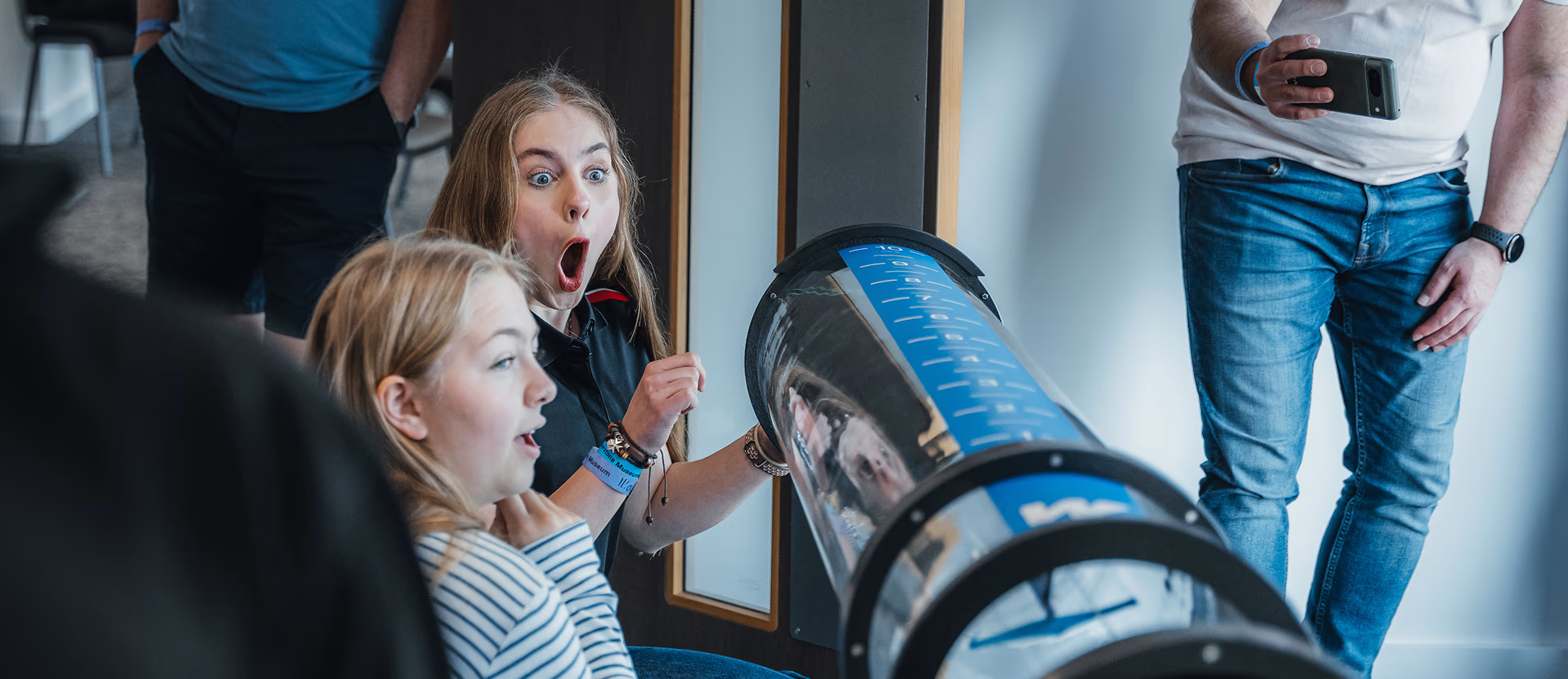 Two young students looking surprised and excited while observing a science experiment in a clear cylindrical tube at a Silverstone STEM camp.
