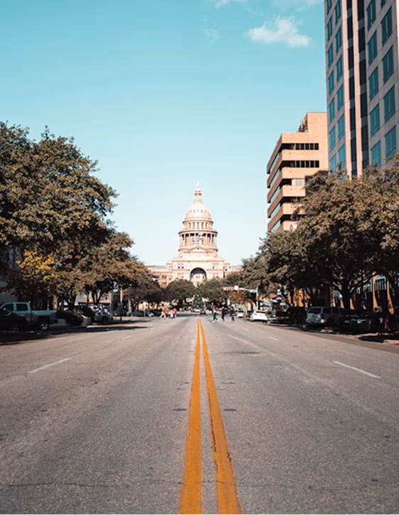 A long, symmetrical view down a wide street leading towards the historic Texas State Capitol building in Austin.