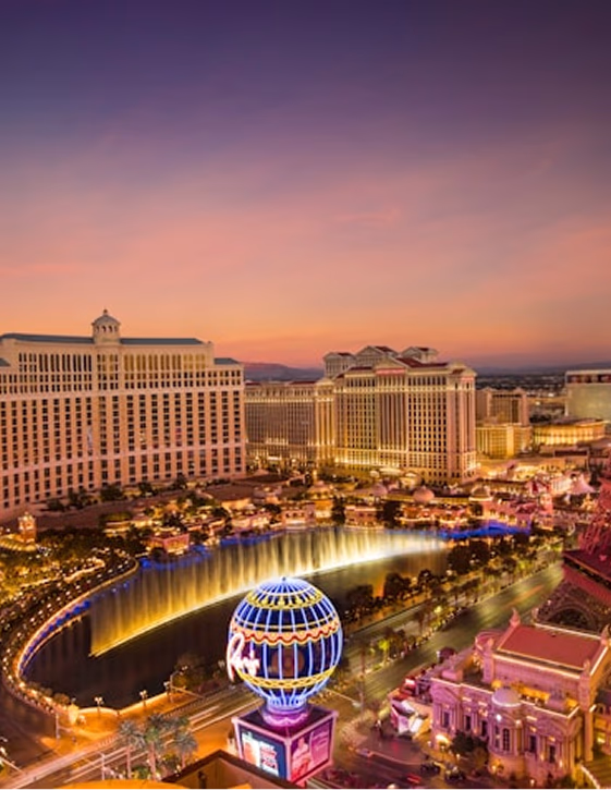 Aerial evening view of the Las Vegas Strip featuring the illuminated Bellagio fountains and bright neon city lights.