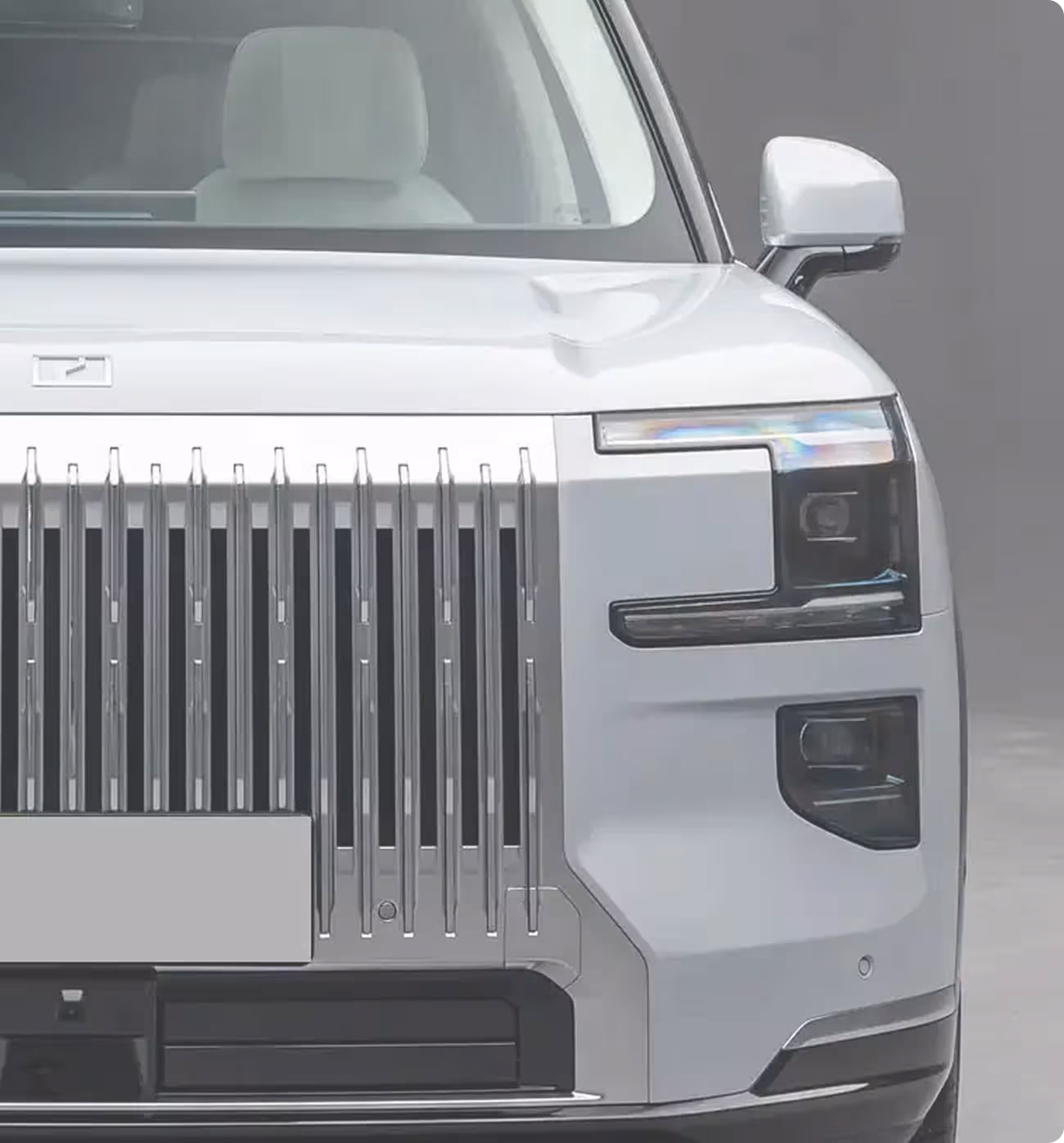 Przód nowoczesnego białego samochodu elektrycznego z chromowanym grillem i unikalnym designem reflektorów.