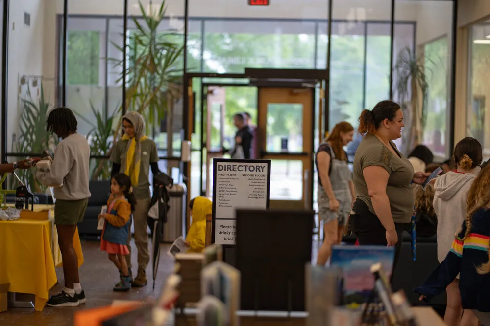 Oxford, Mississippi public library lobby with visitors and families near directory sign, yellow table on left, glass doors