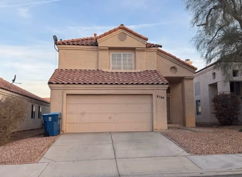 Two-story beige house with a red tile roof and a closed garage door, with a concrete driveway and a blue recycling bin on the left side.