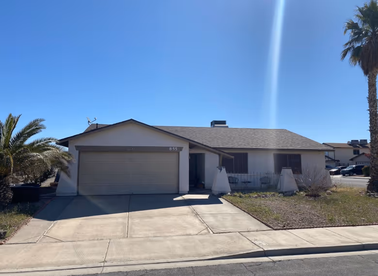 Single-story suburban house with a two-car garage, palm trees, and a clear blue sky.