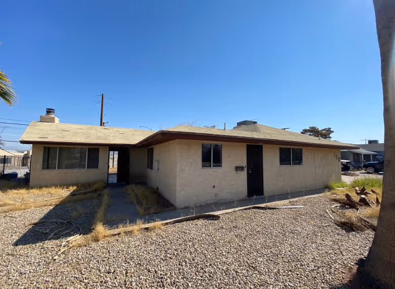 Single-story beige house with a gravel front yard and a clear blue sky.