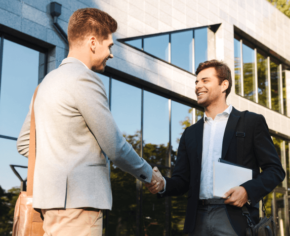 Two businessmen shaking hands in front of a modern office building.