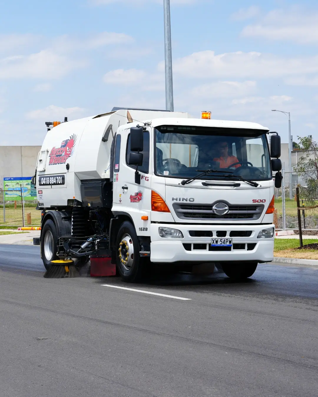 Street cleaner in blue uniform sweeping fallen autumn leaves on a city sidewalk.