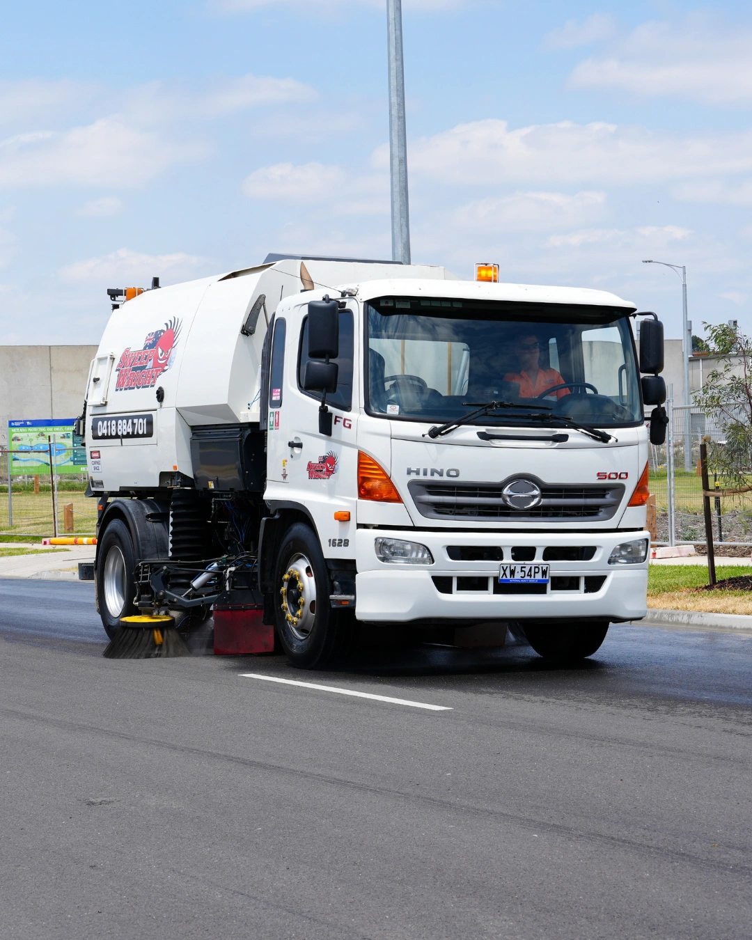 White street sweeper truck cleaning a paved road under a partly cloudy sky.