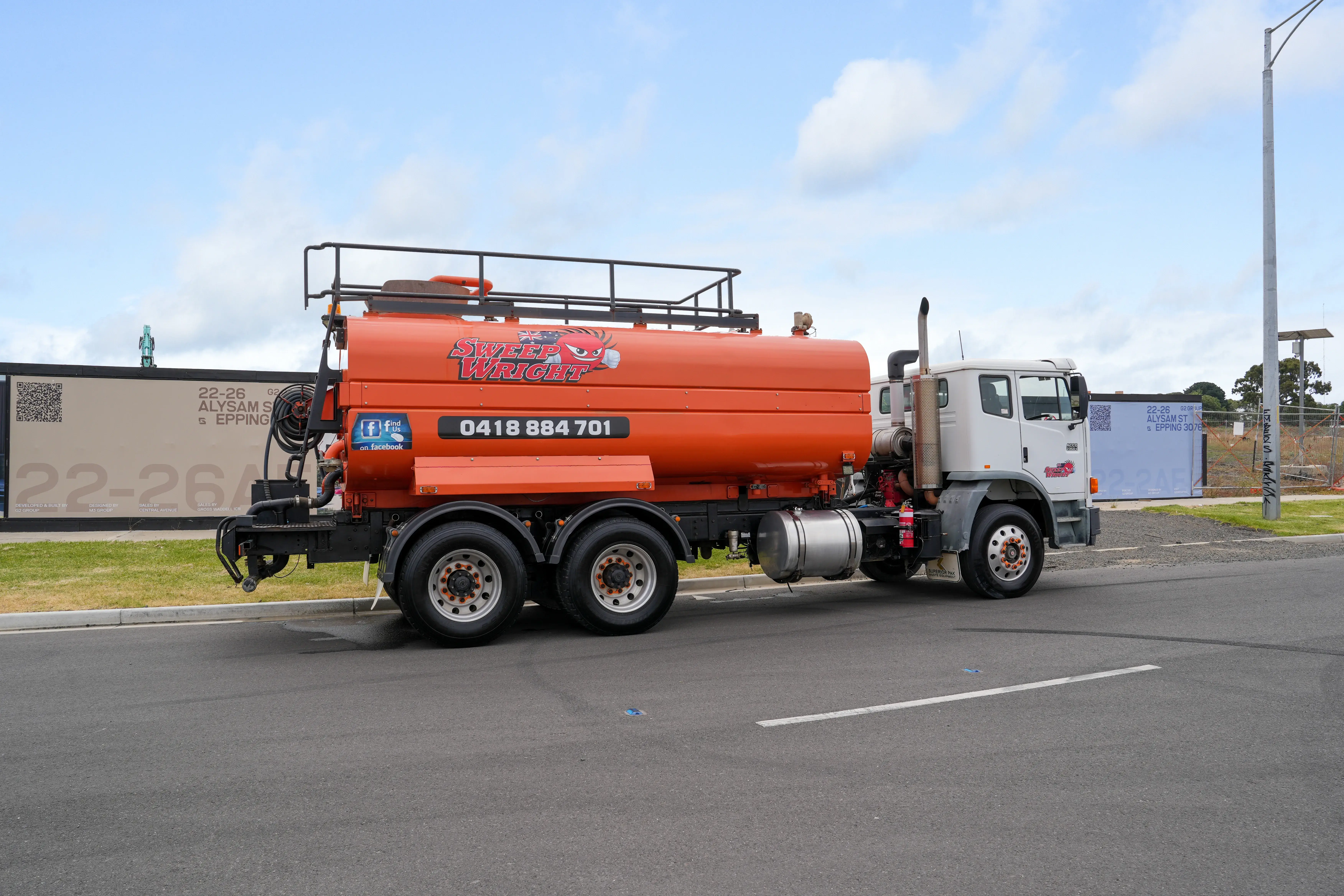 Orange and white Sweep Wright street cleaning truck parked on a roadside with a clear sky background.