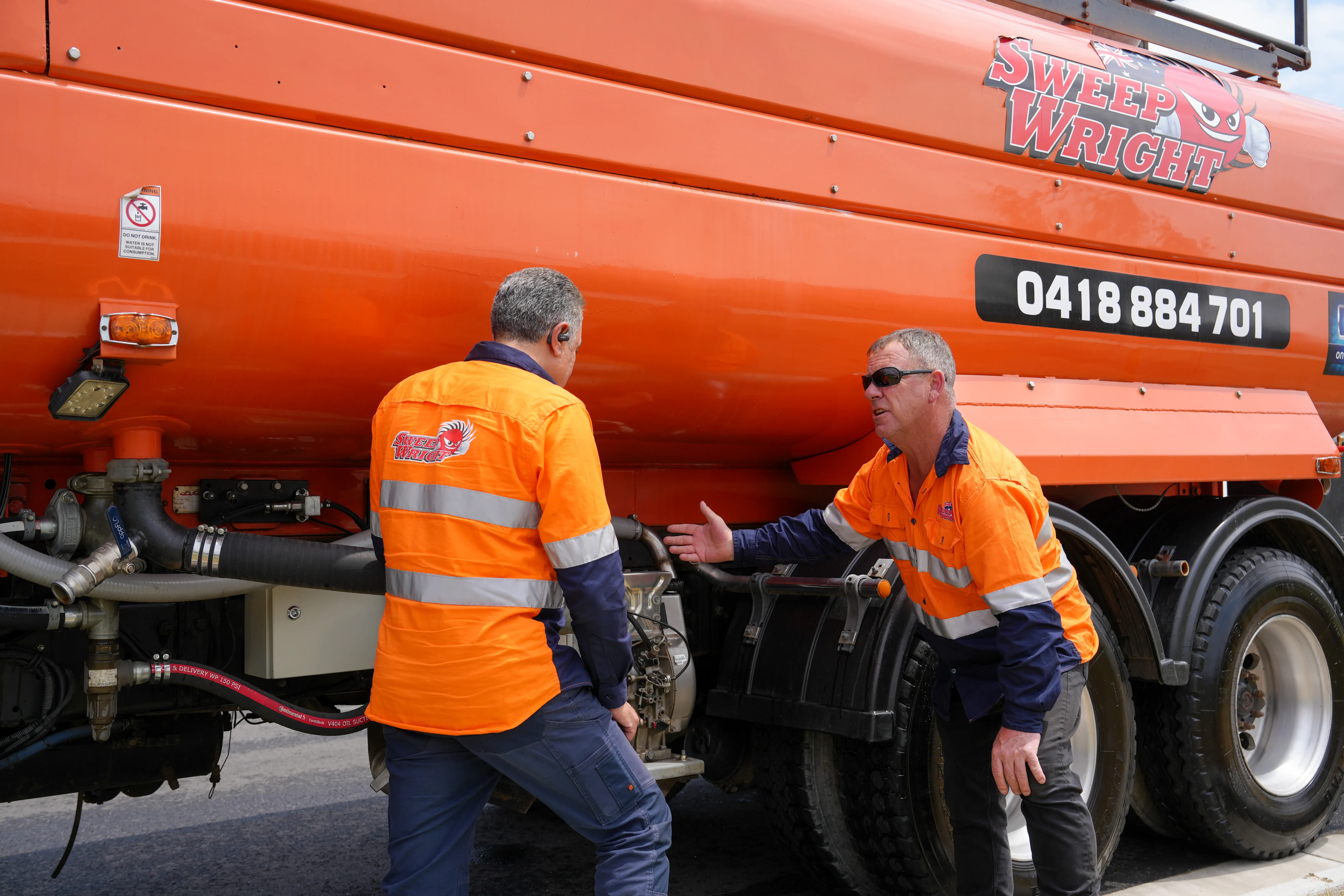 Two men in high-visibility orange work shirts standing next to an orange Sweep Wright truck discussing.