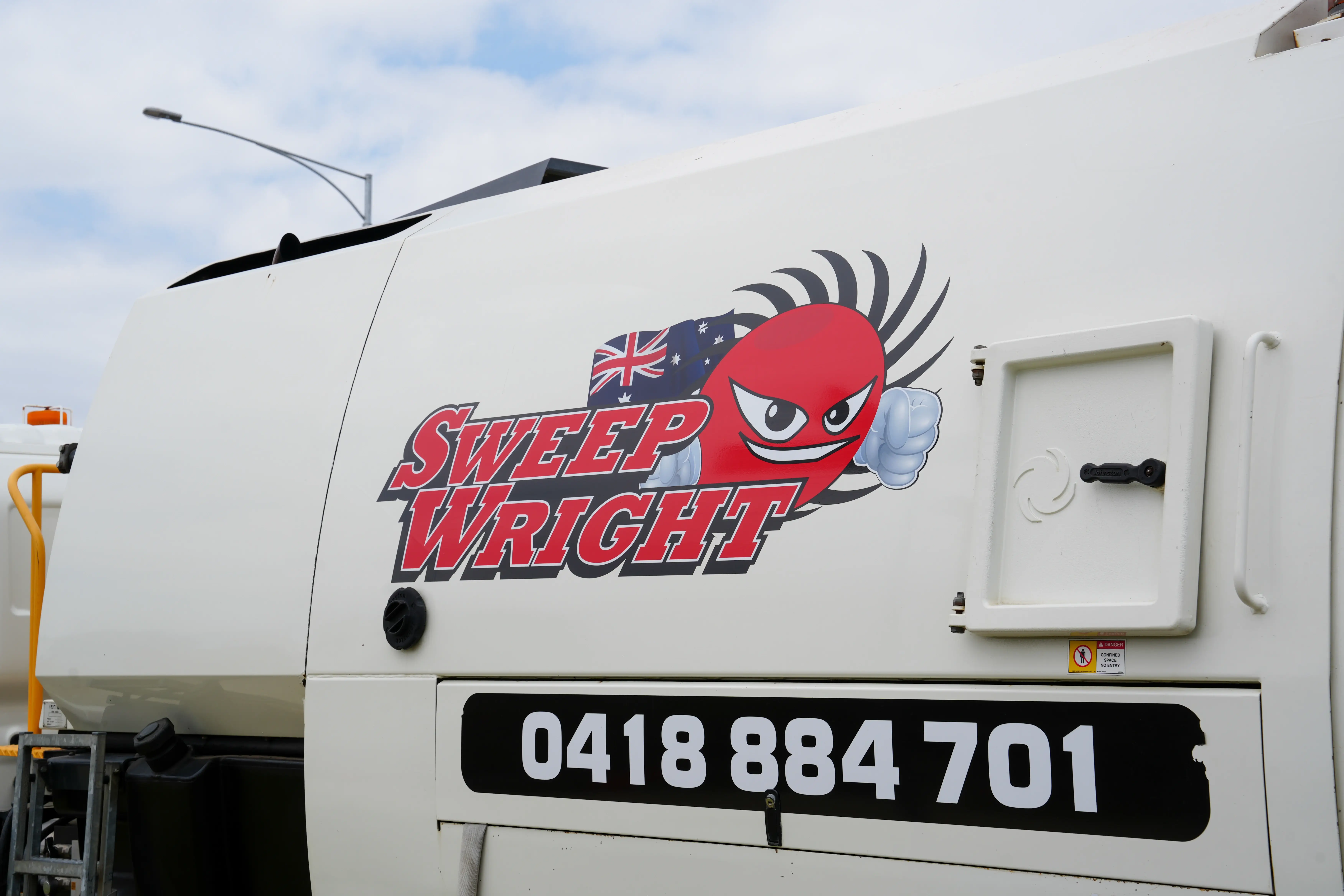 Side view of a white vehicle with a Sweep Wright logo featuring a red cartoon face with fists and an Australian flag, and a phone number below.