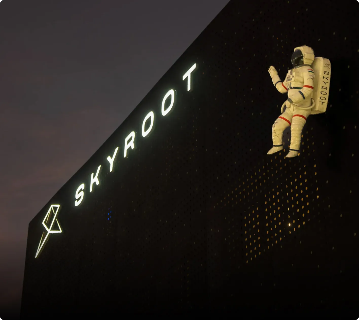 Modern dark perforated building with an astronaut sculpture mounted on the side and the Skyroot Aerospace logo.