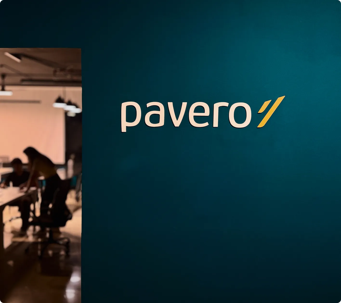 Modern office space with multiple desks, chairs, computers, and overhead fluorescent lighting.