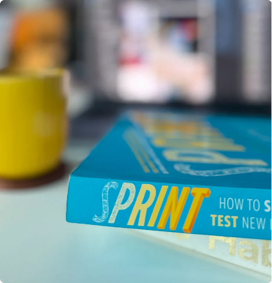 Close-up of the book titled 'Sprint' lying on a white surface with a yellow cup blurred in the background.